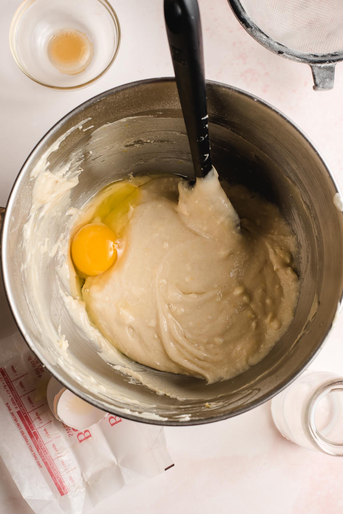 Egg being stirred into cake batter in a stainless steel bowl.