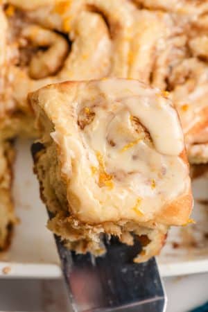 Spatula lifting an orange roll from a casserole dish.