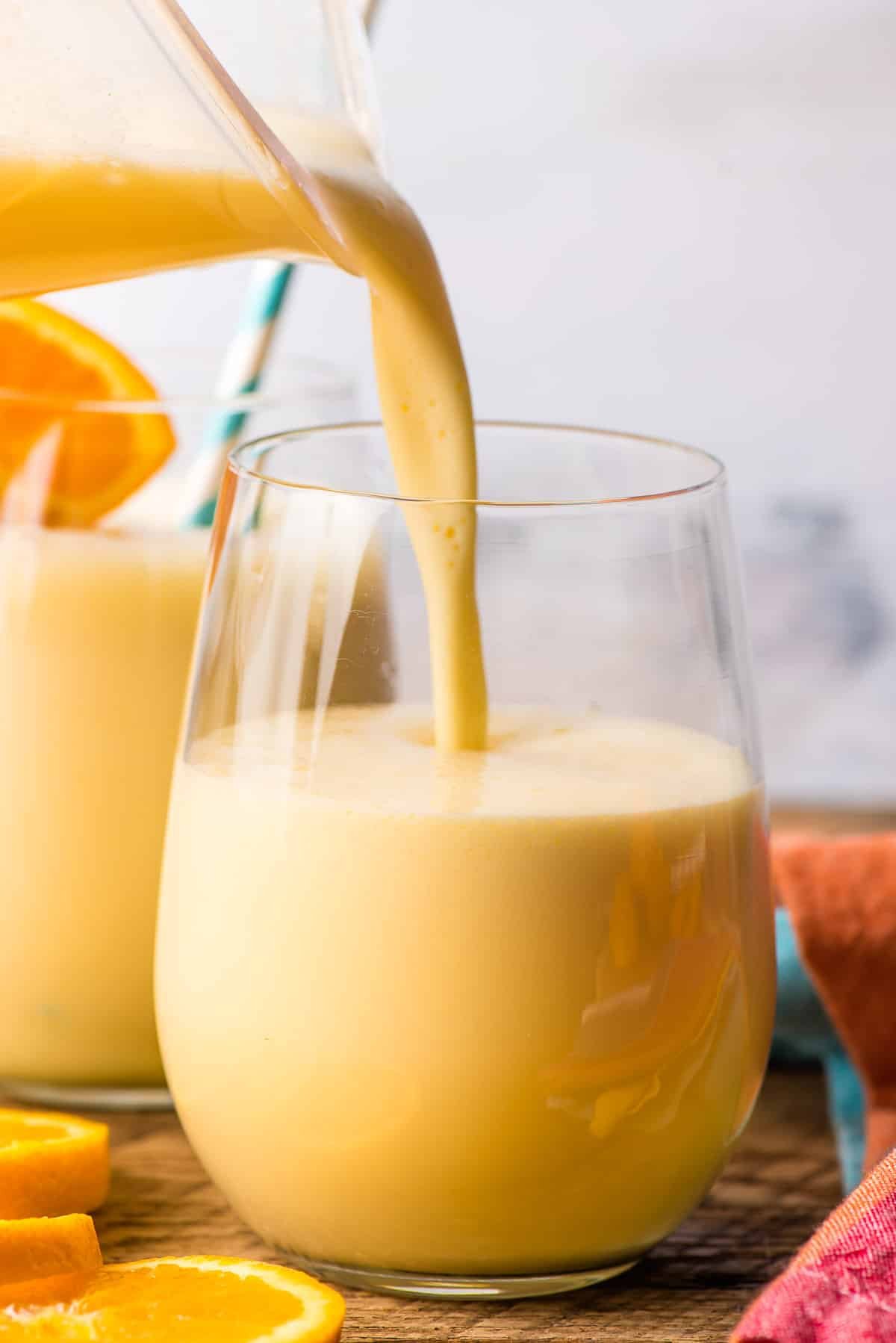 Blender pouring orange julius into a glass cup.