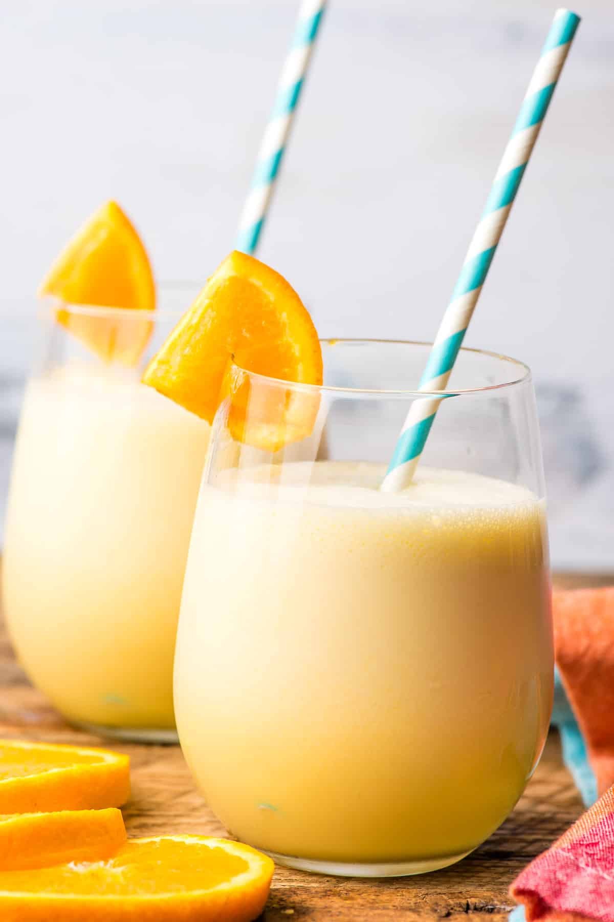 Two glasses of orange julius with orange wedges on the side.
