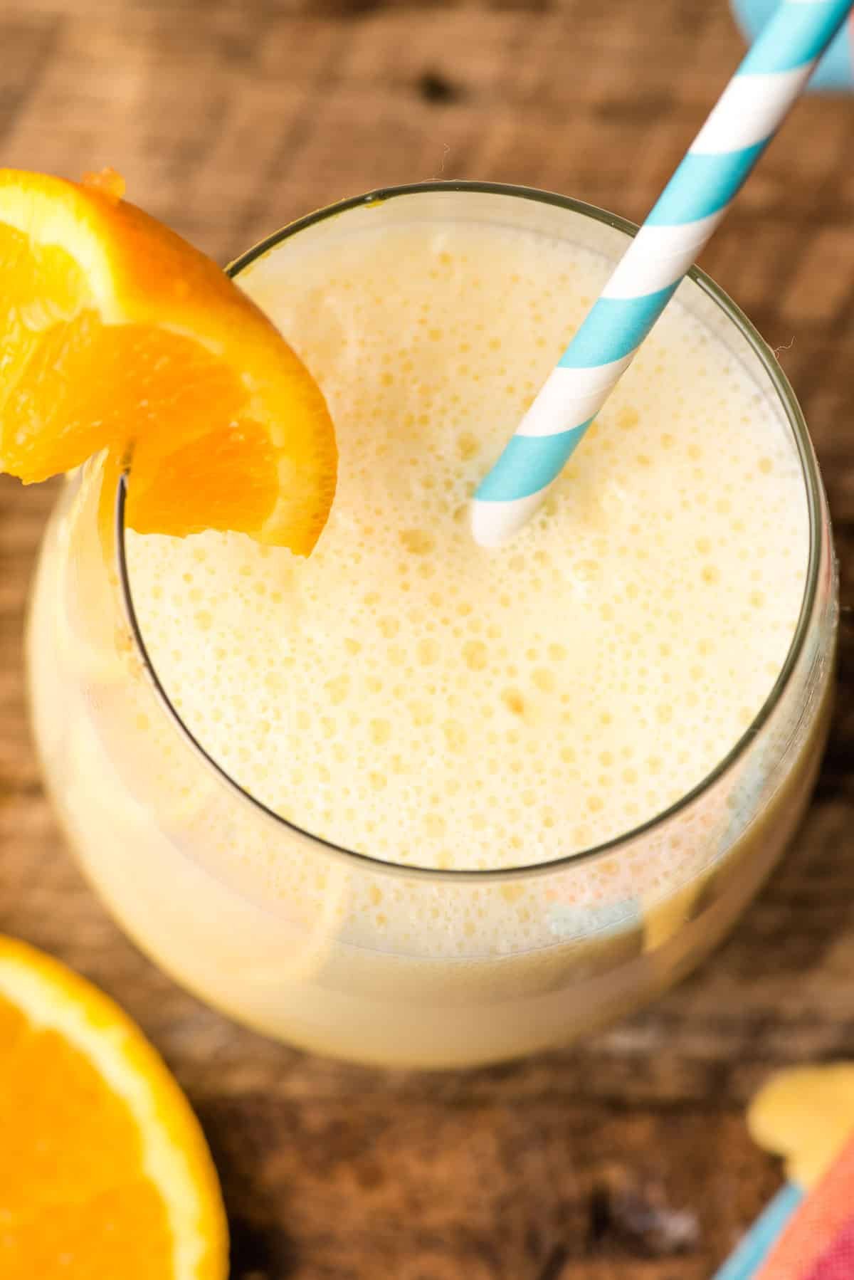 Frothy top of a glass of orange julius, with a blue and white striped straw stuck in it.