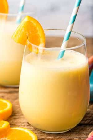 Glass of orange julius with orange wedge and blue and white striped paper straw.
