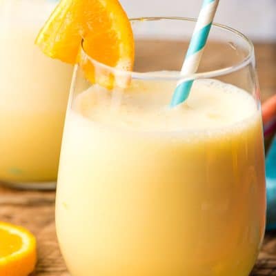Glass of orange julius with orange wedge and blue and white striped paper straw.