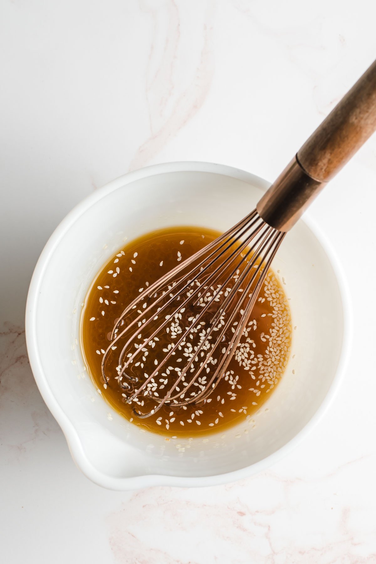 Asian sesame dressing shown in a white bowl with a whisk.