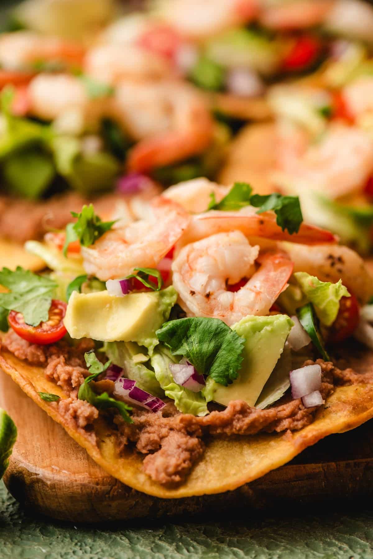 Shrimp tostadas stacked with refried beans, avocado, tomato, red onion, jalapeno, and cilantro.
