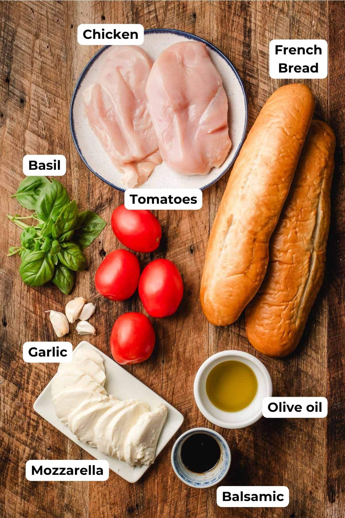 Chicken breasts, basil, tomato, mozzarella, balsamic, olive oil, and French bread on a wood background.