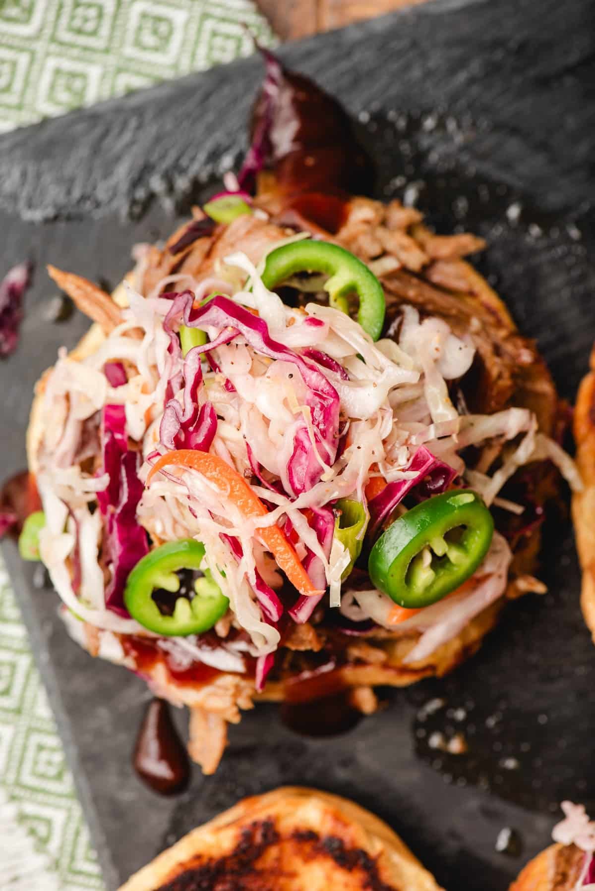 Open face pulled pork sandwich topped with coleslaw and jalapenos.