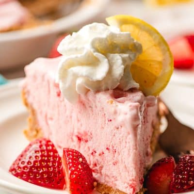 Slice of strawberry lemonade pie on a white plate, surrounded by strawberries.