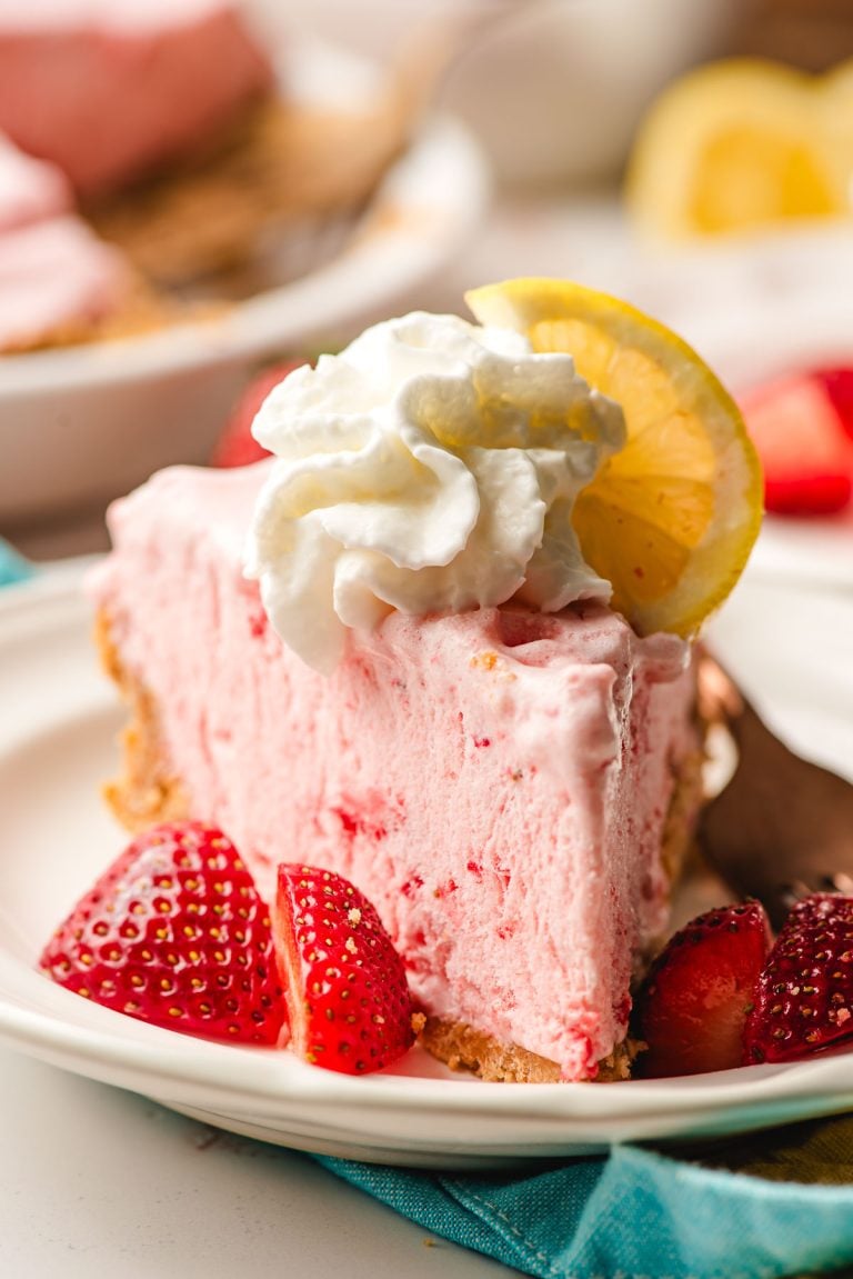 Slice of strawberry lemonade pie on a white plate, surrounded by strawberries.