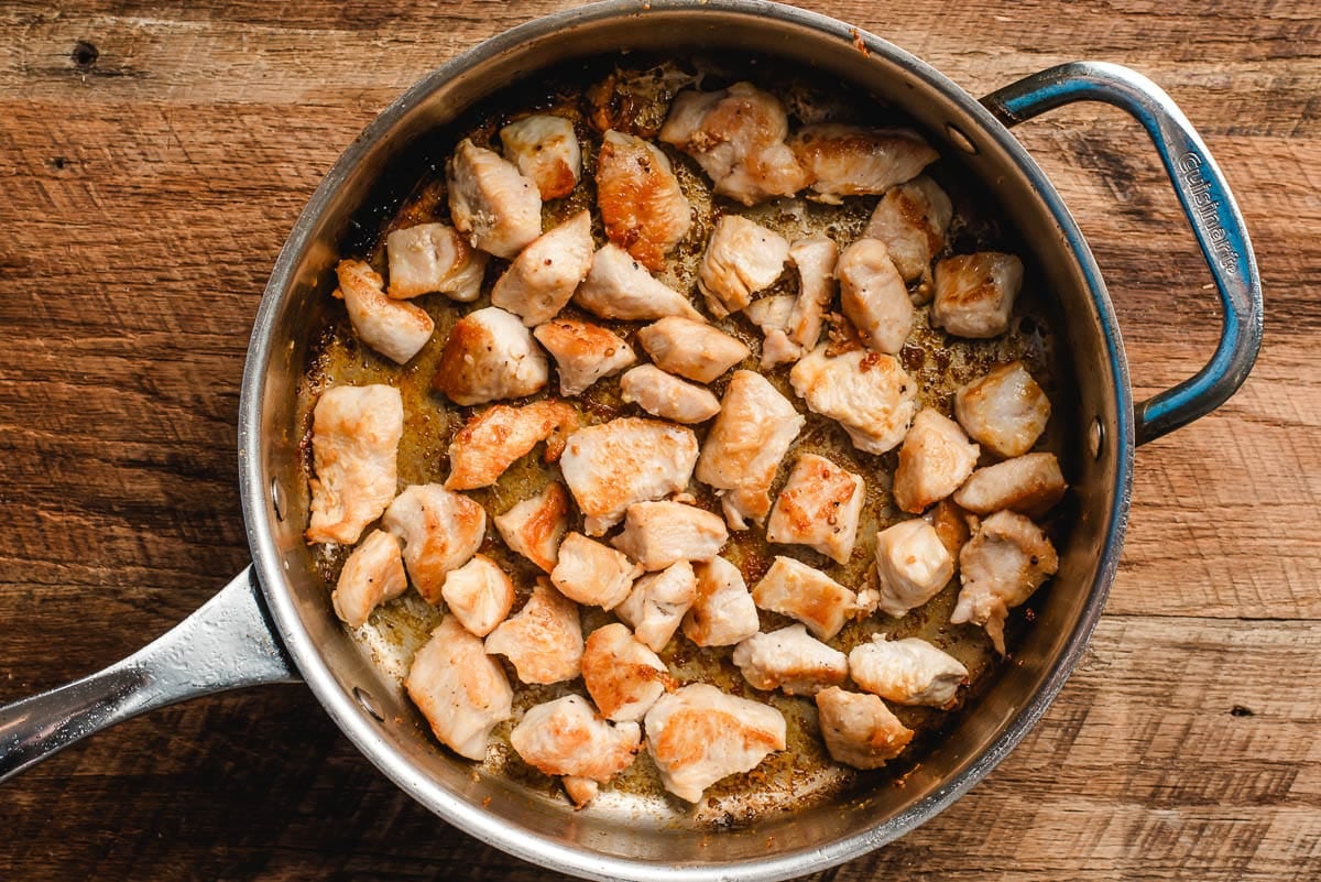 Chopped chicken breast browned in a large stainless steel skillet.