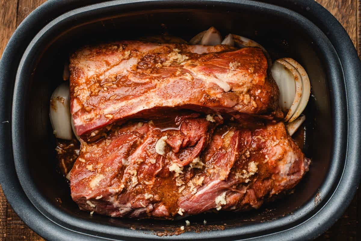 Pork shoulder topped with a sweet and spicy rub in a crock pot.