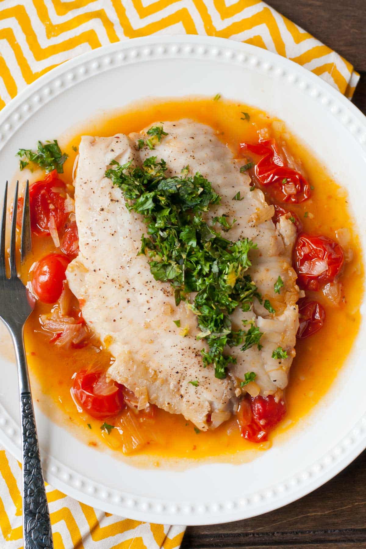 Poached tilapia on top of a tomato wine goop on a white plate.