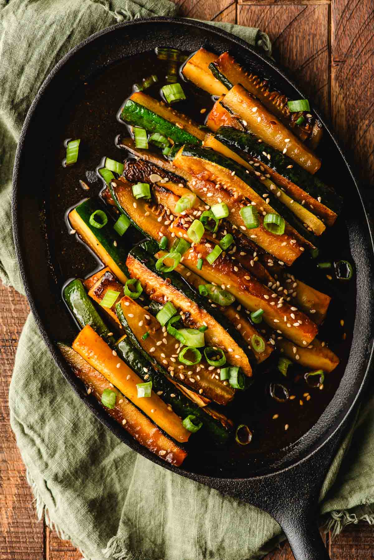 Asian zucchini spears topped with sesame seeds and green onion on a cast iron platter.