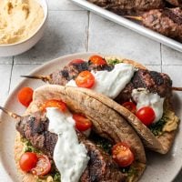 Two pita sandwiches filled with beef kofta, cherry tomatoes, tabbouleh, and tzatziki.
