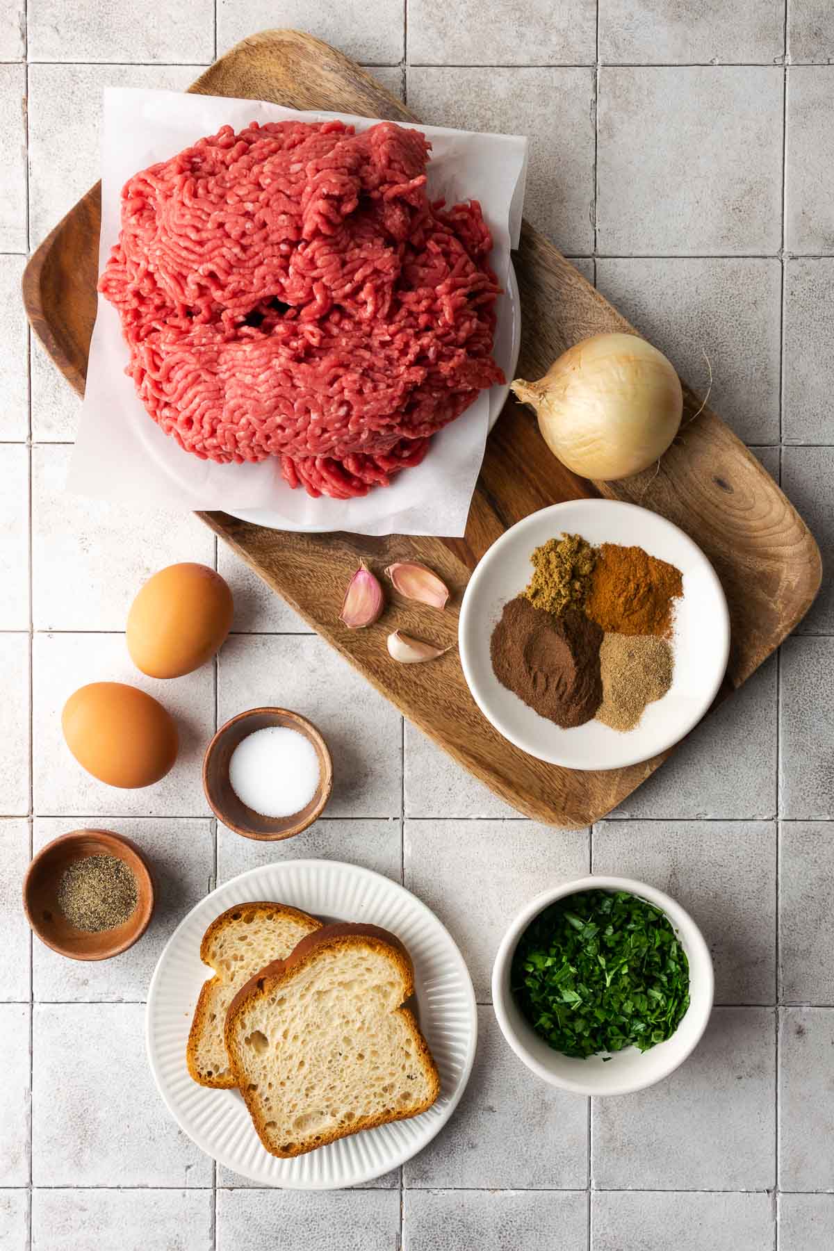 Ingredients for beef kofta displayed on a gray tile background.