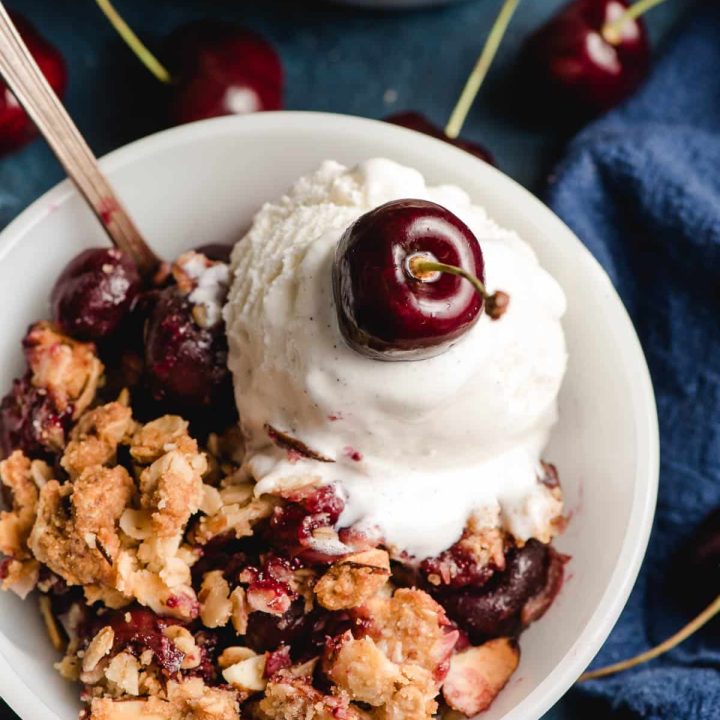 Cherry crumble in a bowl with a scoop of ice cream and cherry on top.