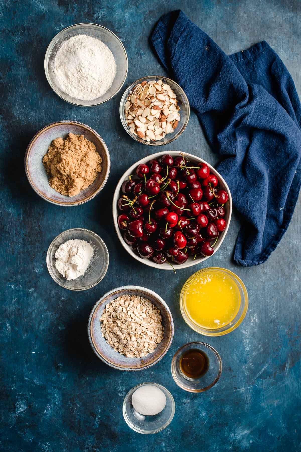 Ingredients for fresh cherry crumble displayed in prep bowls on a undecorous background.