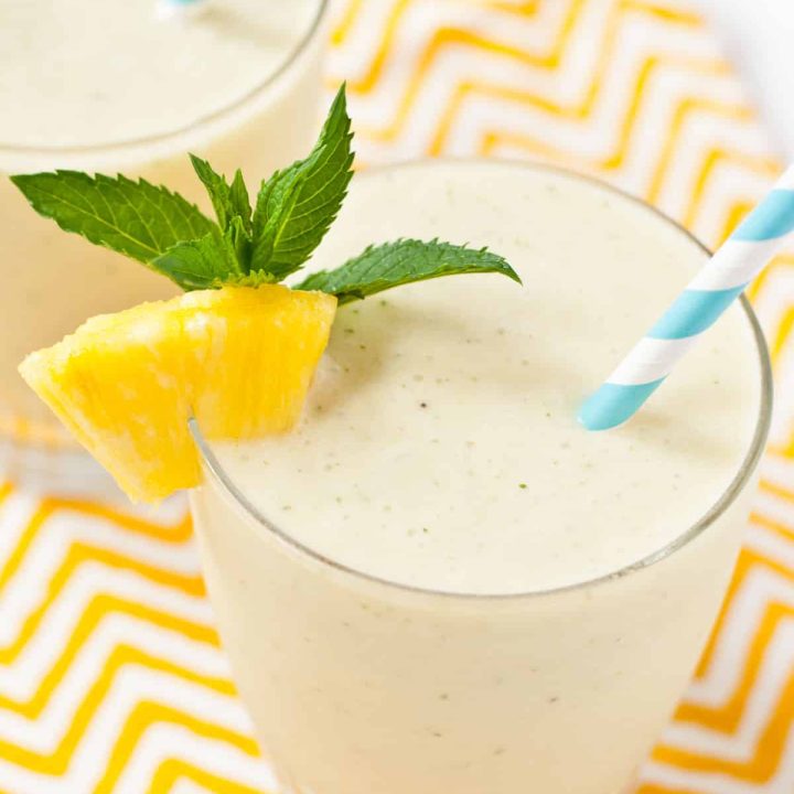 Pineapple and banana smoothie with a mint leaf garnish and blue and white paper straw.