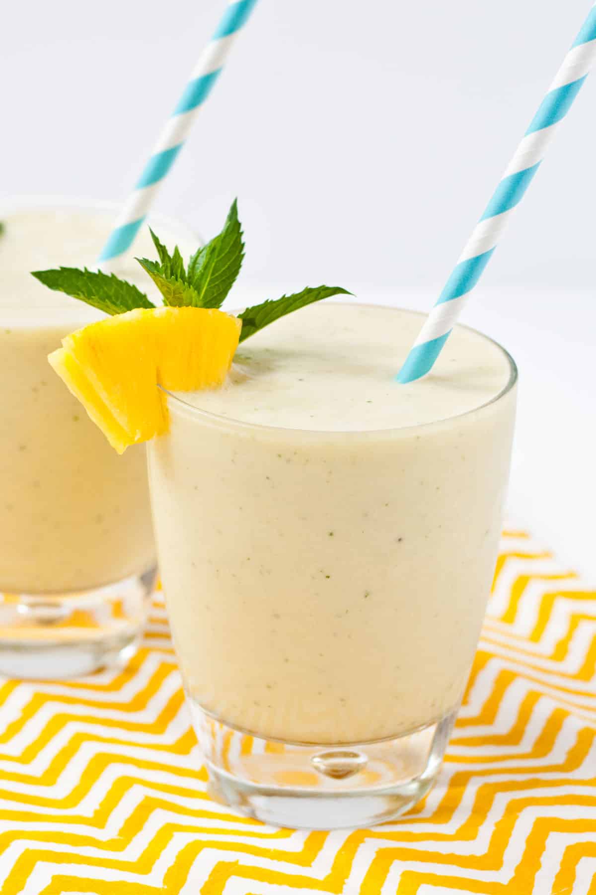 Banana and pineapple smoothie in a glass with a blue and white paper straw.