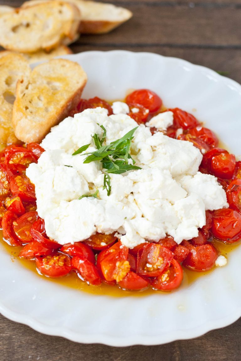 Bowl of roasted tomatoes topped with goat cheese and crostini.