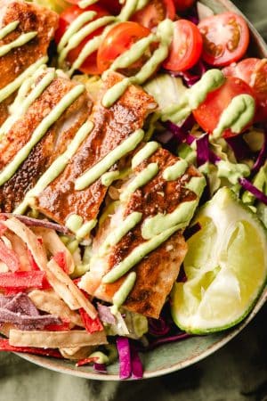 Fish taco salad bowls with lime wedge and drizzle of avocado dressing.