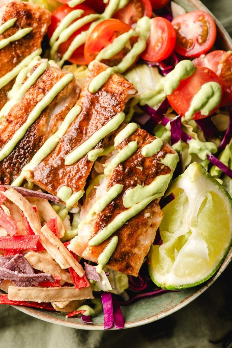 Fish taco salad bowls with lime wedge and drizzle of avocado dressing.