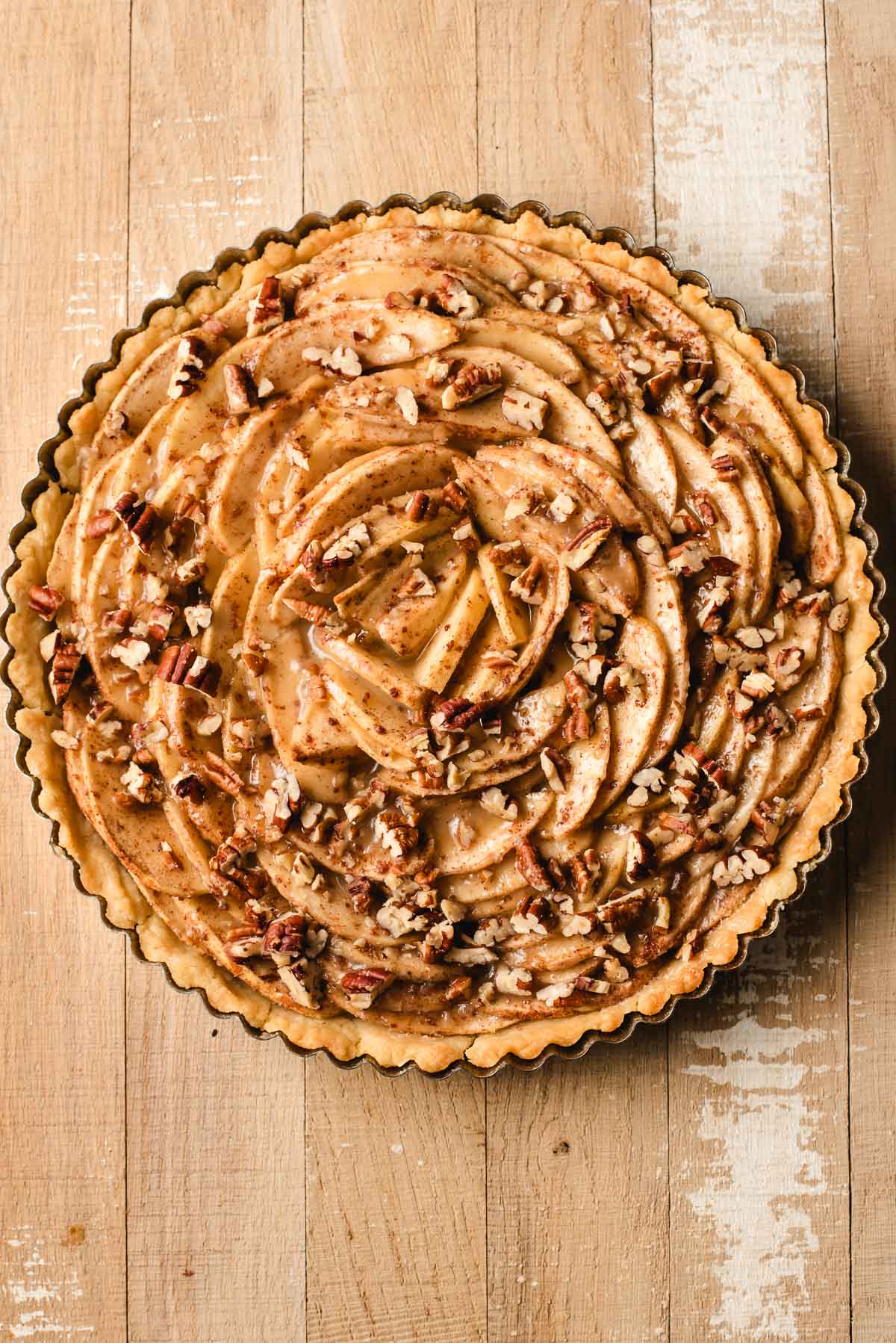 Tart pan filled with sliced apples, spices, caramel sauce, and pecans.