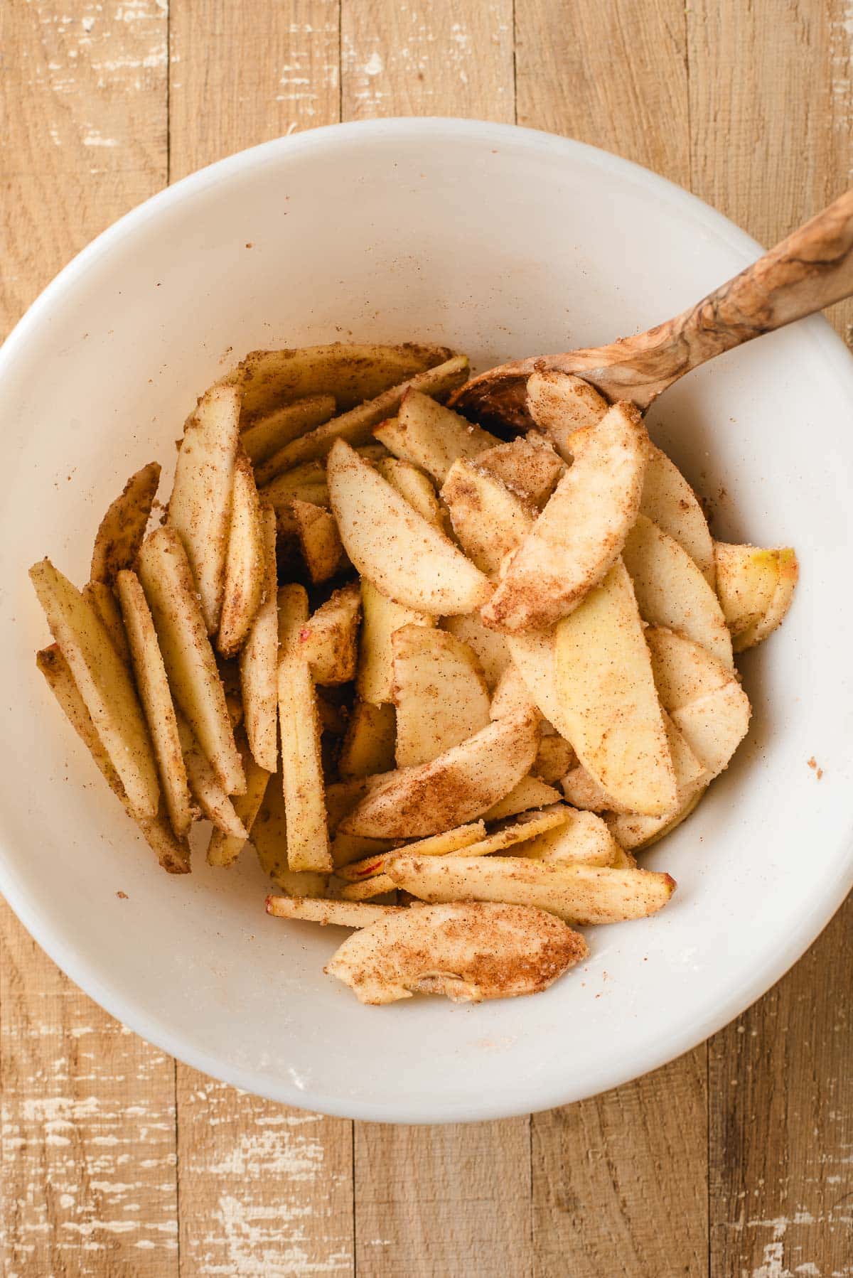 Sliced apples tossed with cinnamon, cardamom, and brown sugar in a bowl.