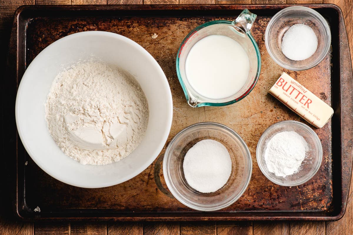 Ingredients in drop biscuits arranged in prep bowls: flour, milk, slat, butter, sugar, and baking powder.