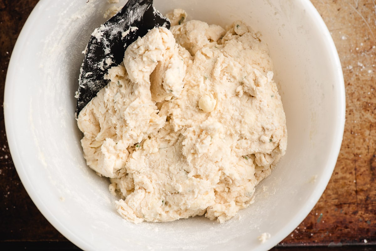 Drop biscuit dough in a white bowl with a black spatula.