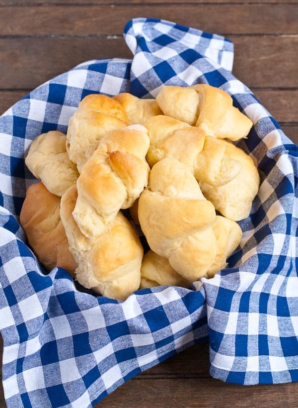 a basket full of butterhorn dinner rolls in a blue gingam napkin