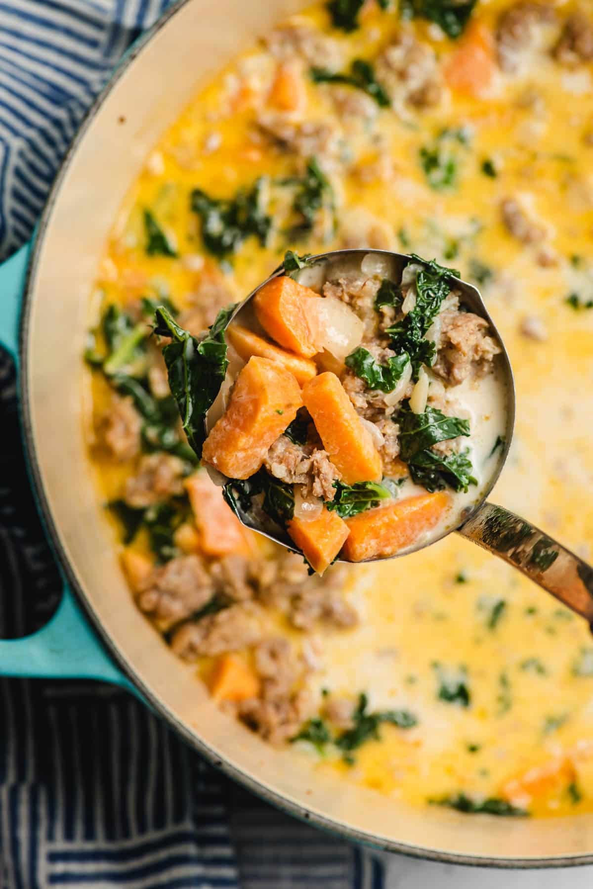 Soup ladle full of creamy sweet potato soup with sausage and kale.