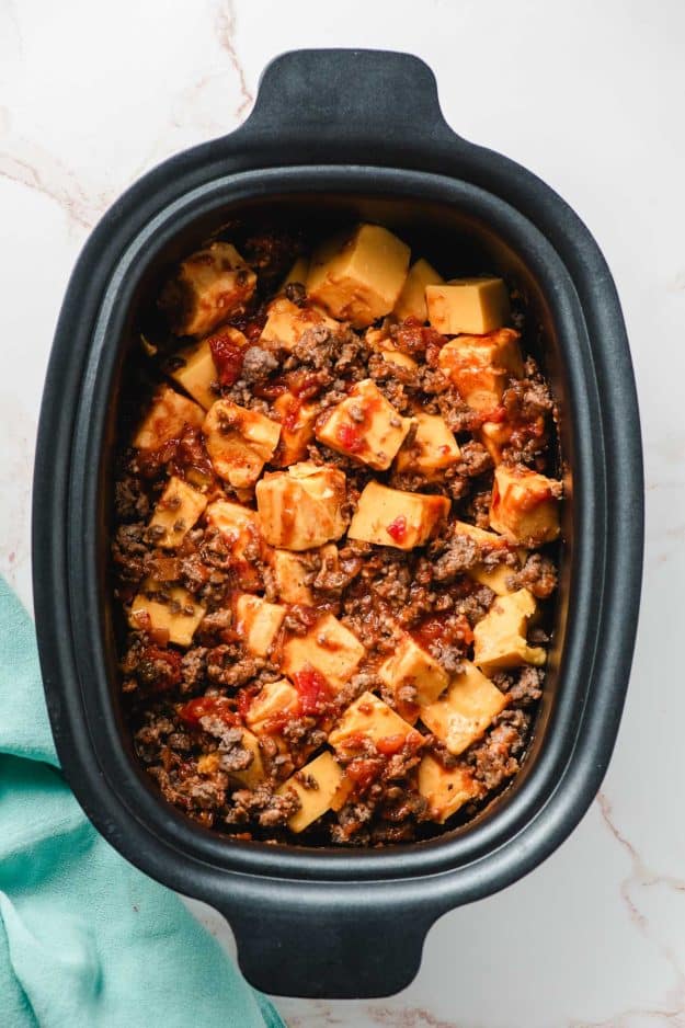 Slow cooker filled with cubed velveeta cheese, salsa, and sausage crumbles.