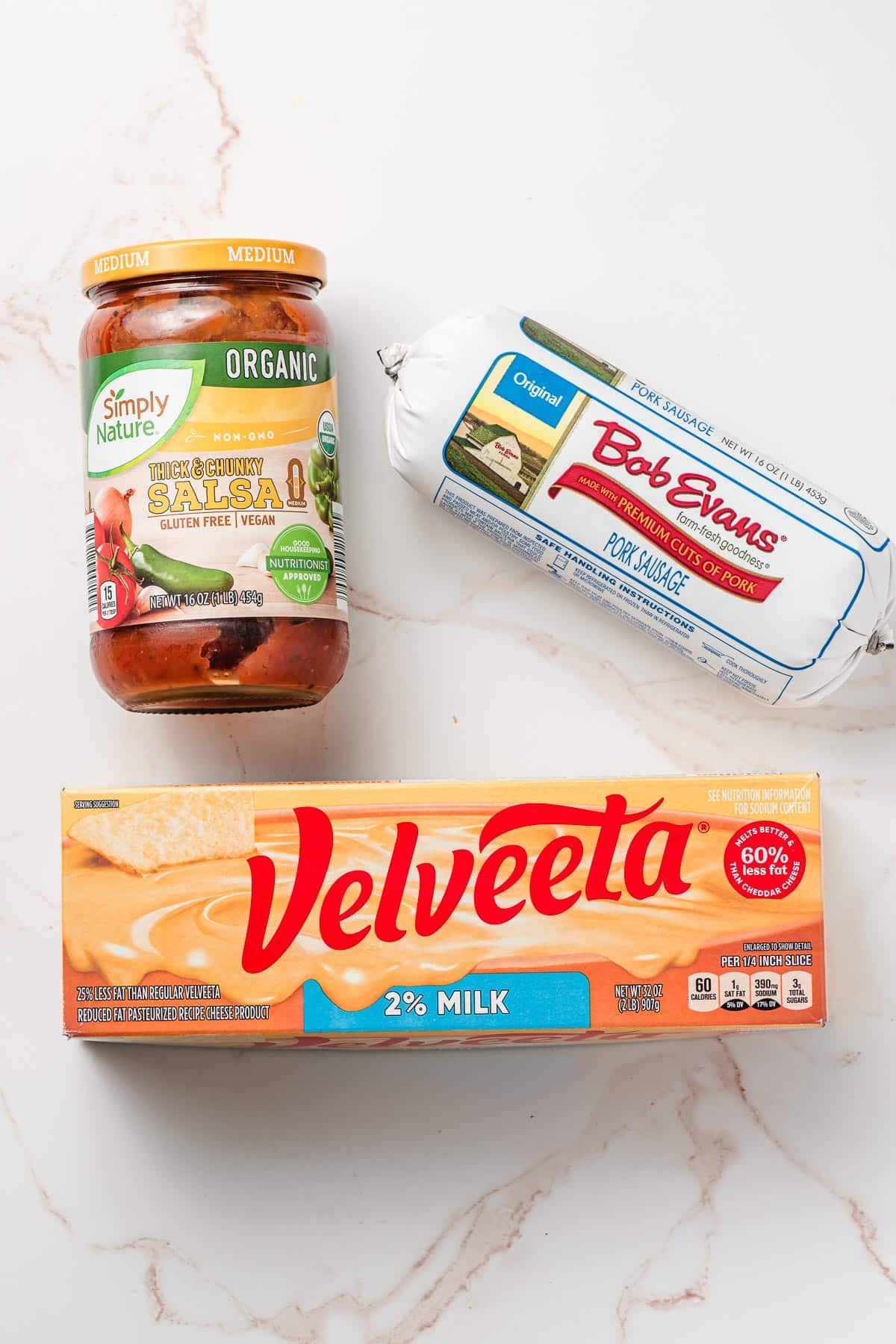 Velveeta cheese, a jar of salsa, and a tube of breakfast sausage on a white background.