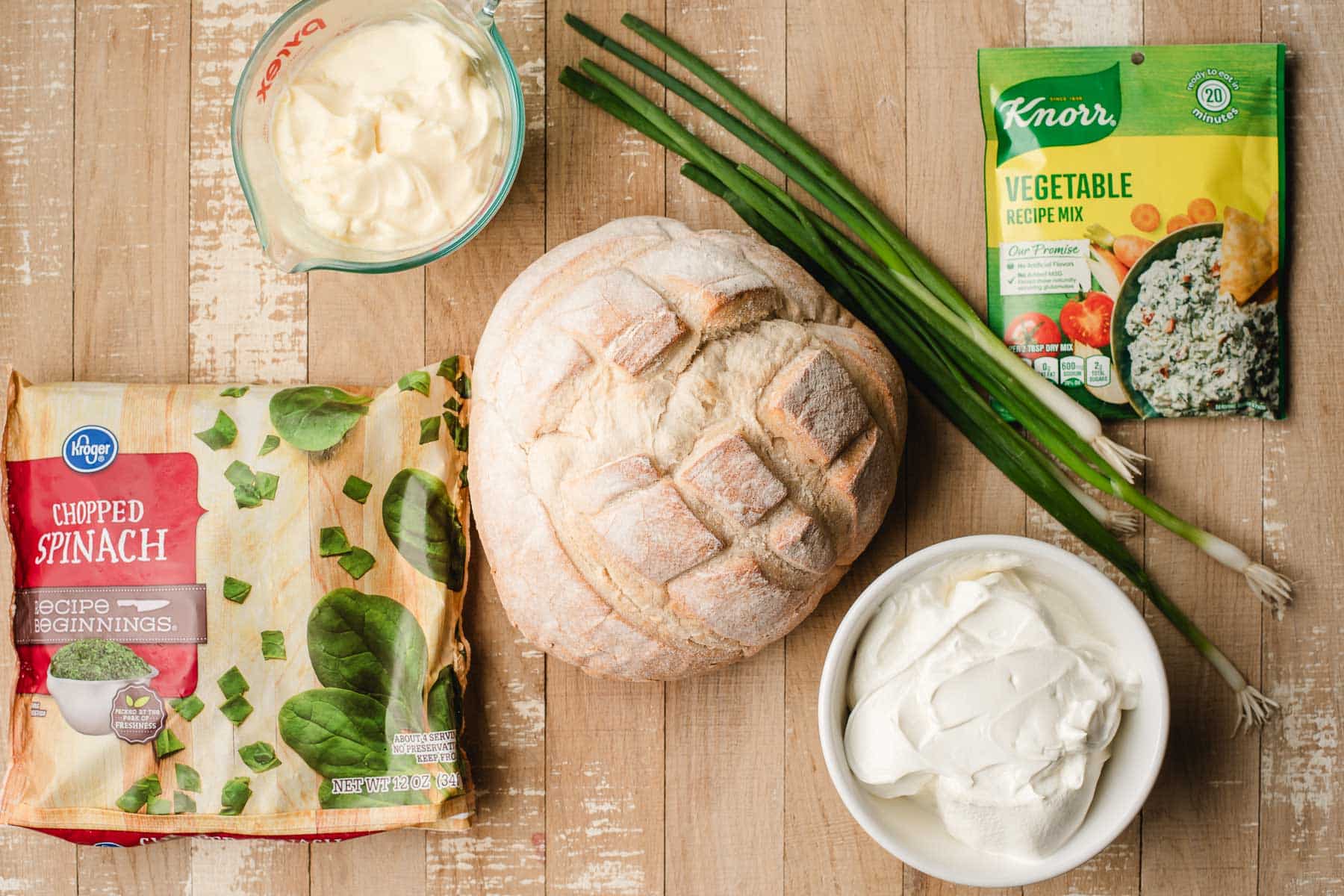 Sourdough bread bowl, frozen spinach, green onions, Knorr vegetable mix, mayonnaise, and sour cream on a wooden background.