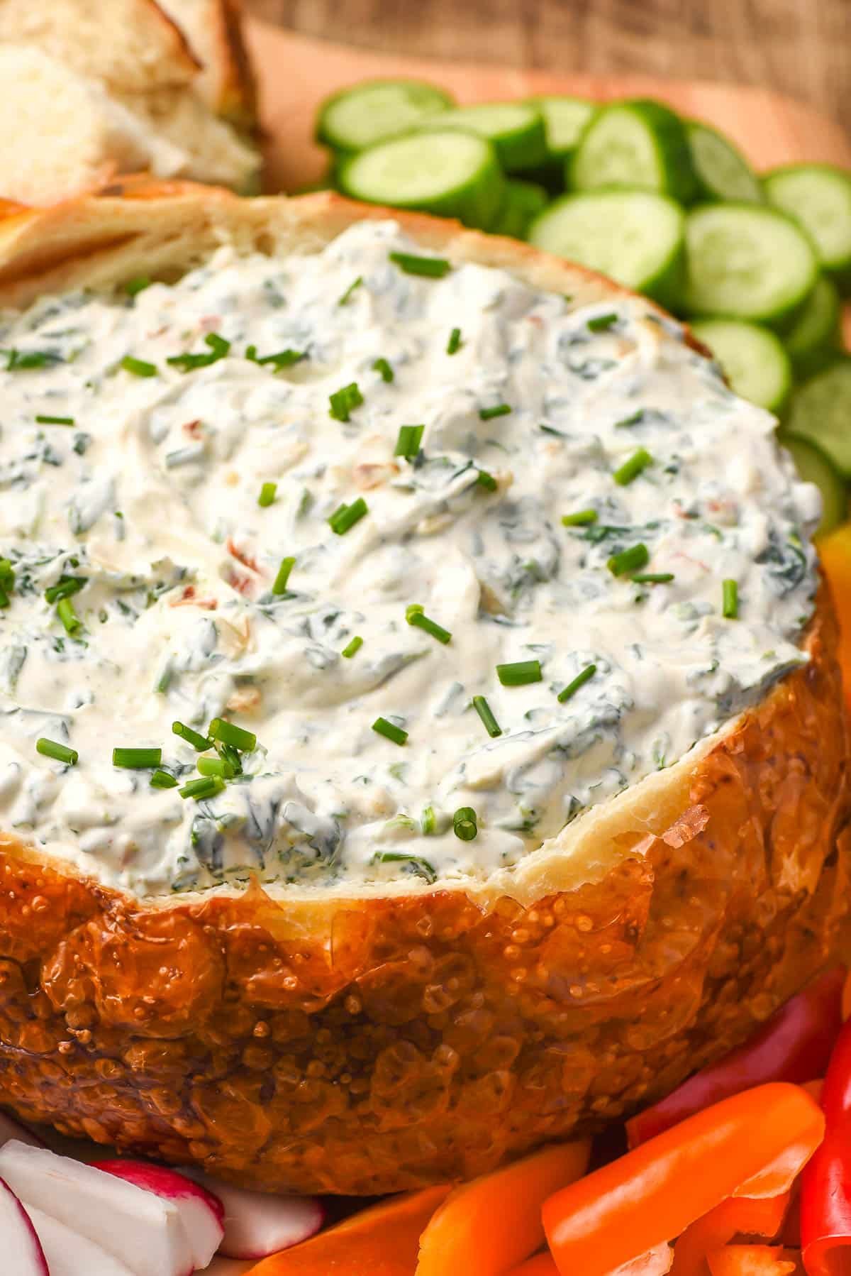 Cold spinach dip in a bread bowl with fresh cut veggies.