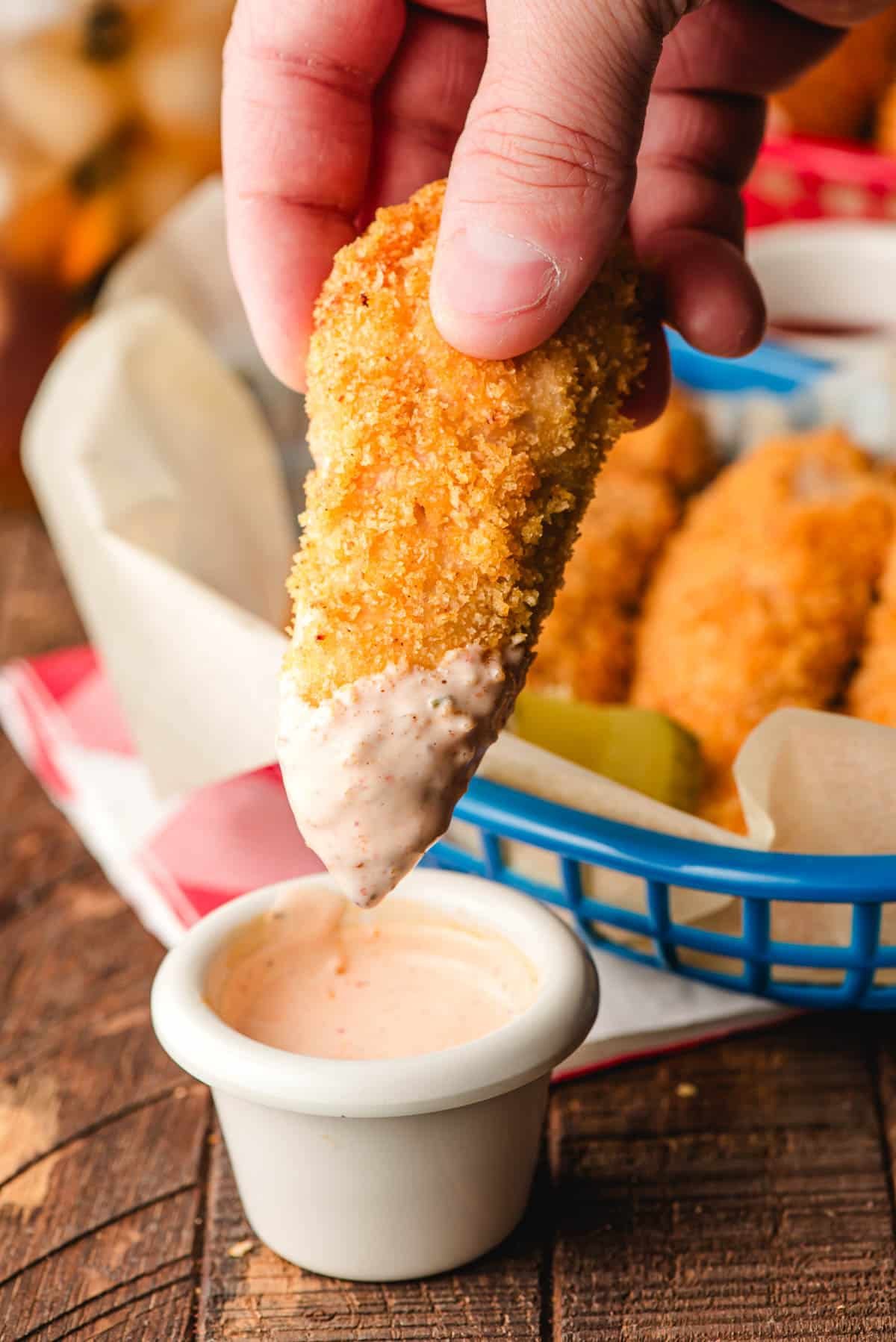 Panko crusted chicken tender being dipped into a cup of Sriracha ranch.