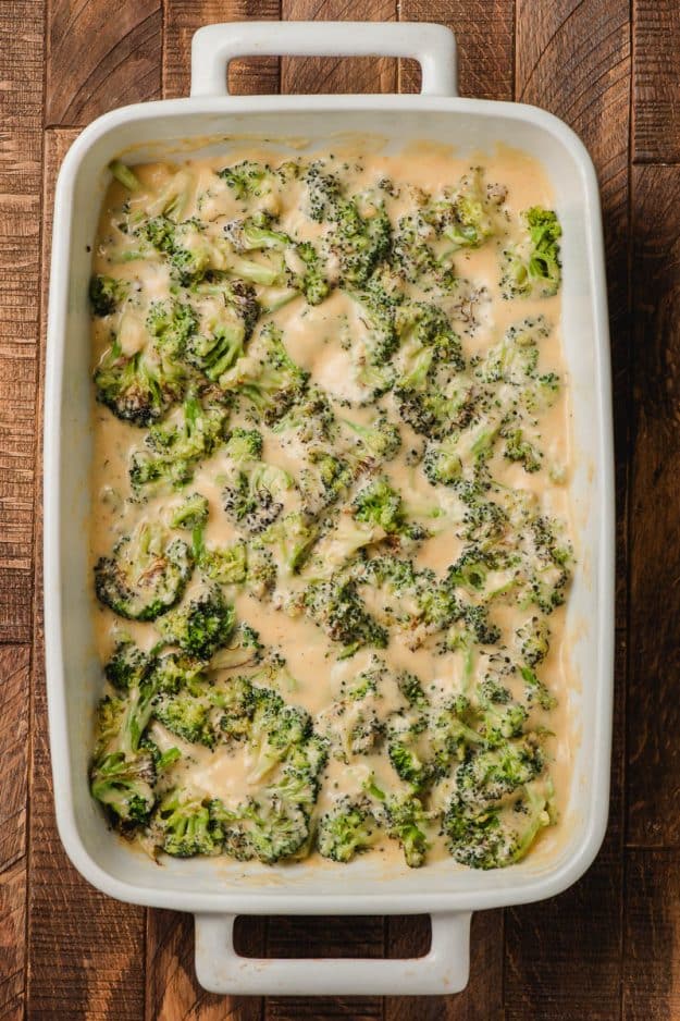 Broccoli tossed with a homemade cheese sauce in a white casserole dish.