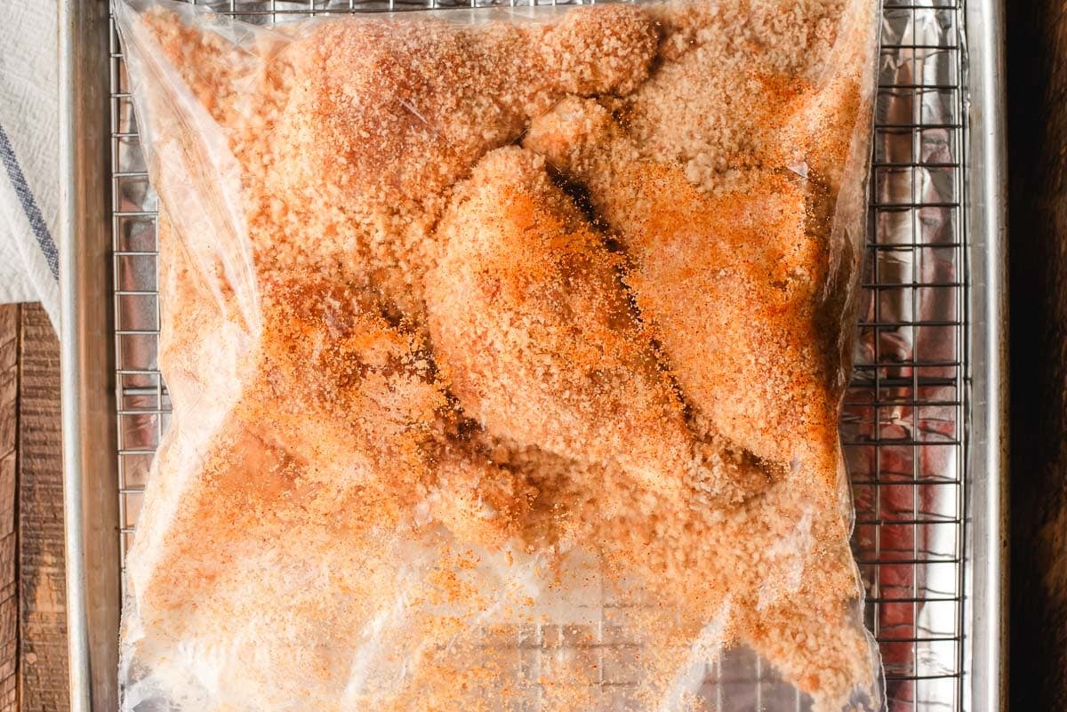 Mayo coated chicken being tossed in a bag of seasoned panko breadcrumbs.