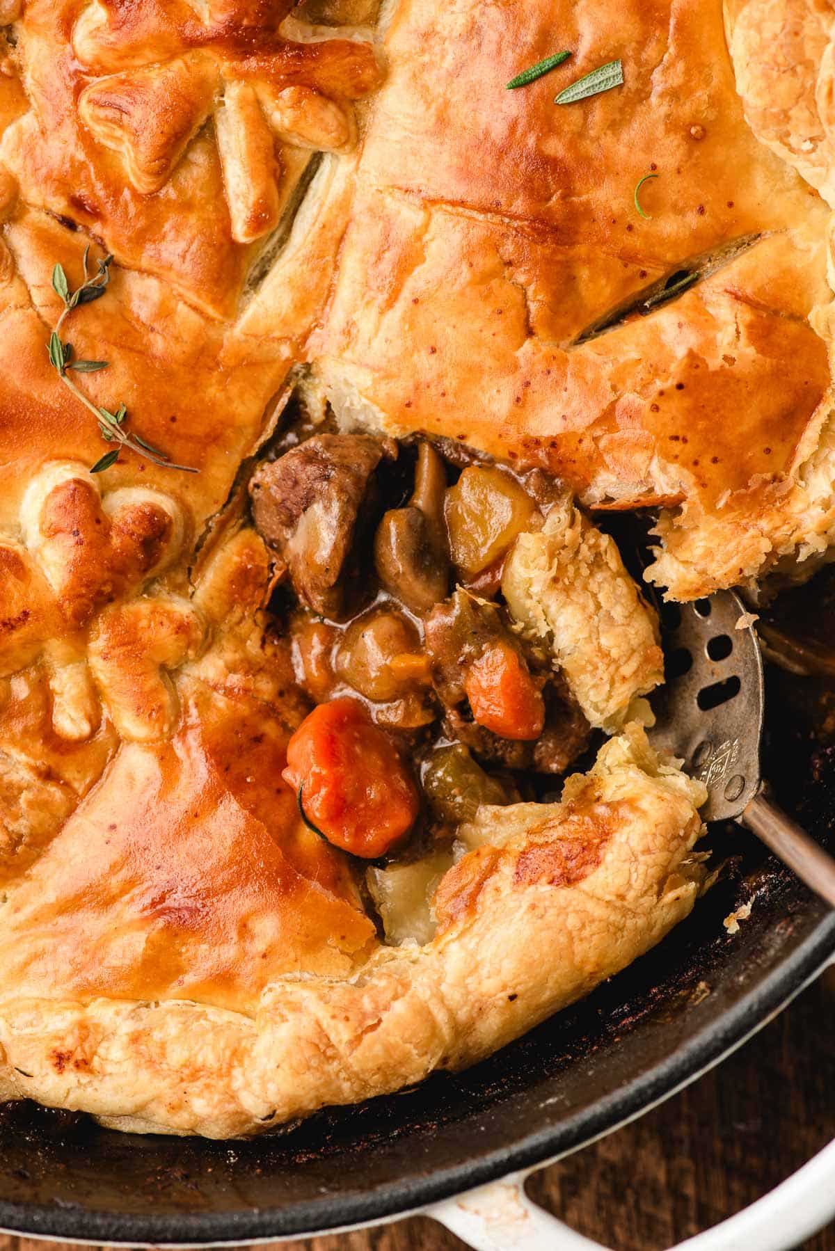 Spoon taking a scoop of beef pot pie out of a cast iron skillet.