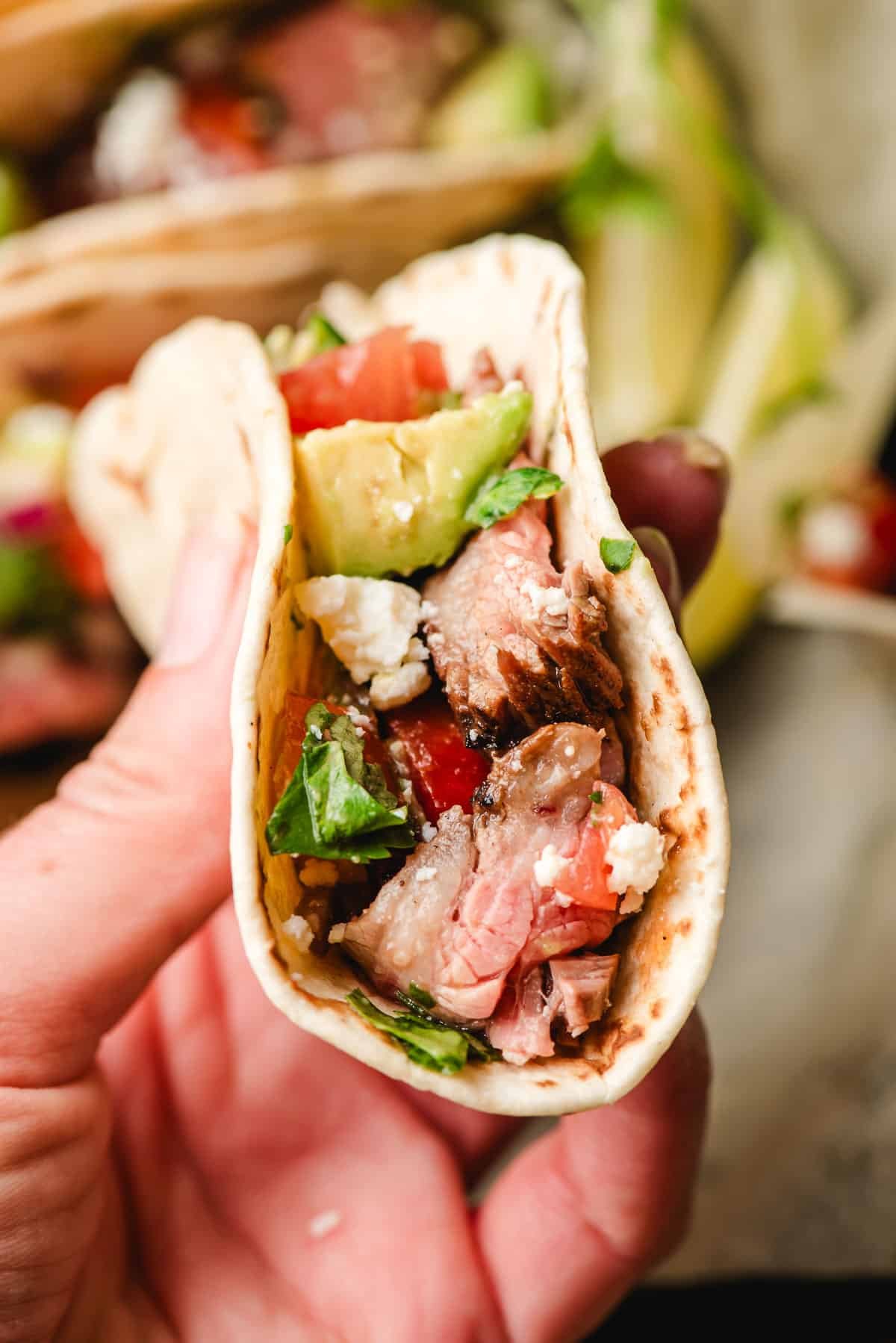 Hand holding a grilled flank steak taco with pico de gallo.
