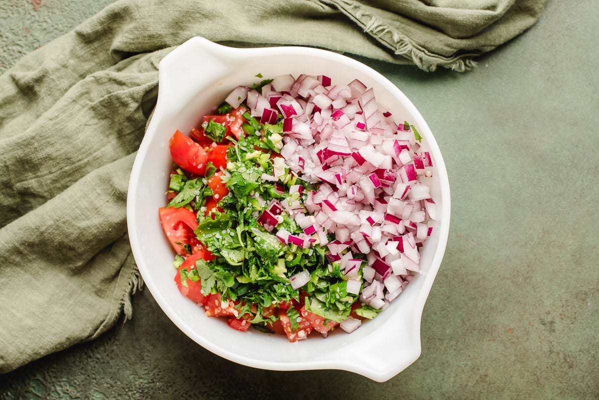 Chopped tomatoes, cilantro, jalapeno, and red onion in a white bowl.
