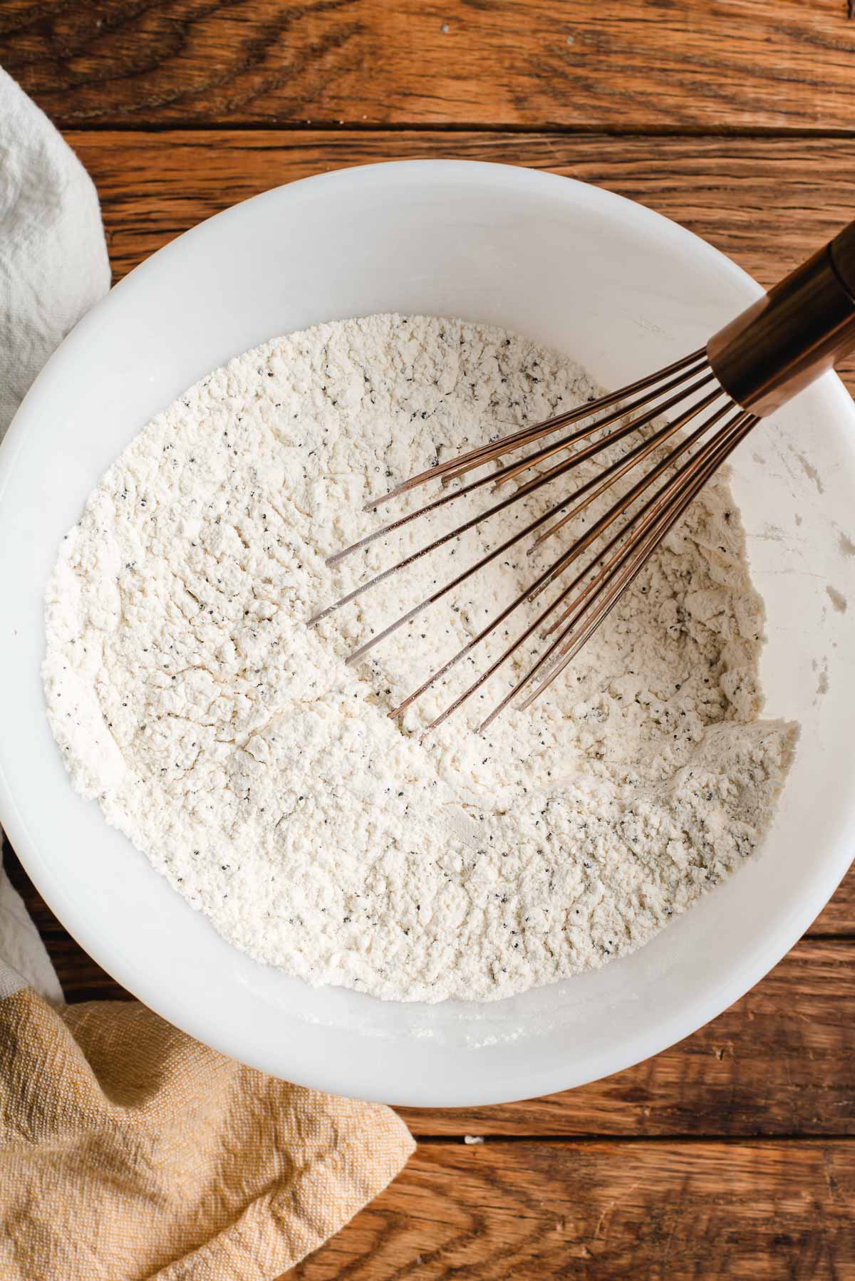 Dry ingredients for muffins in a white mixing bowl with a whisk.