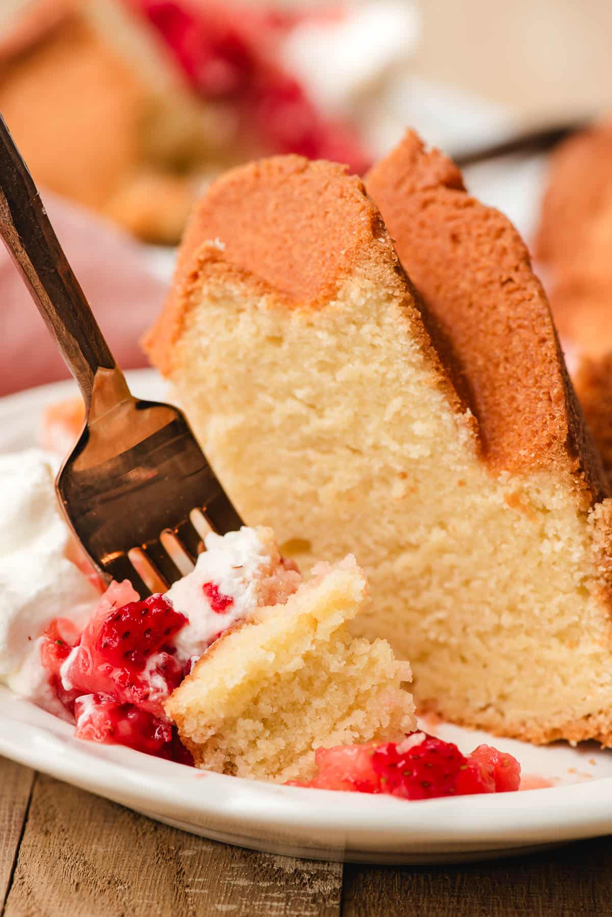 Fork stabbing a bite of pound cake with whipped cream and smashed strawberries.