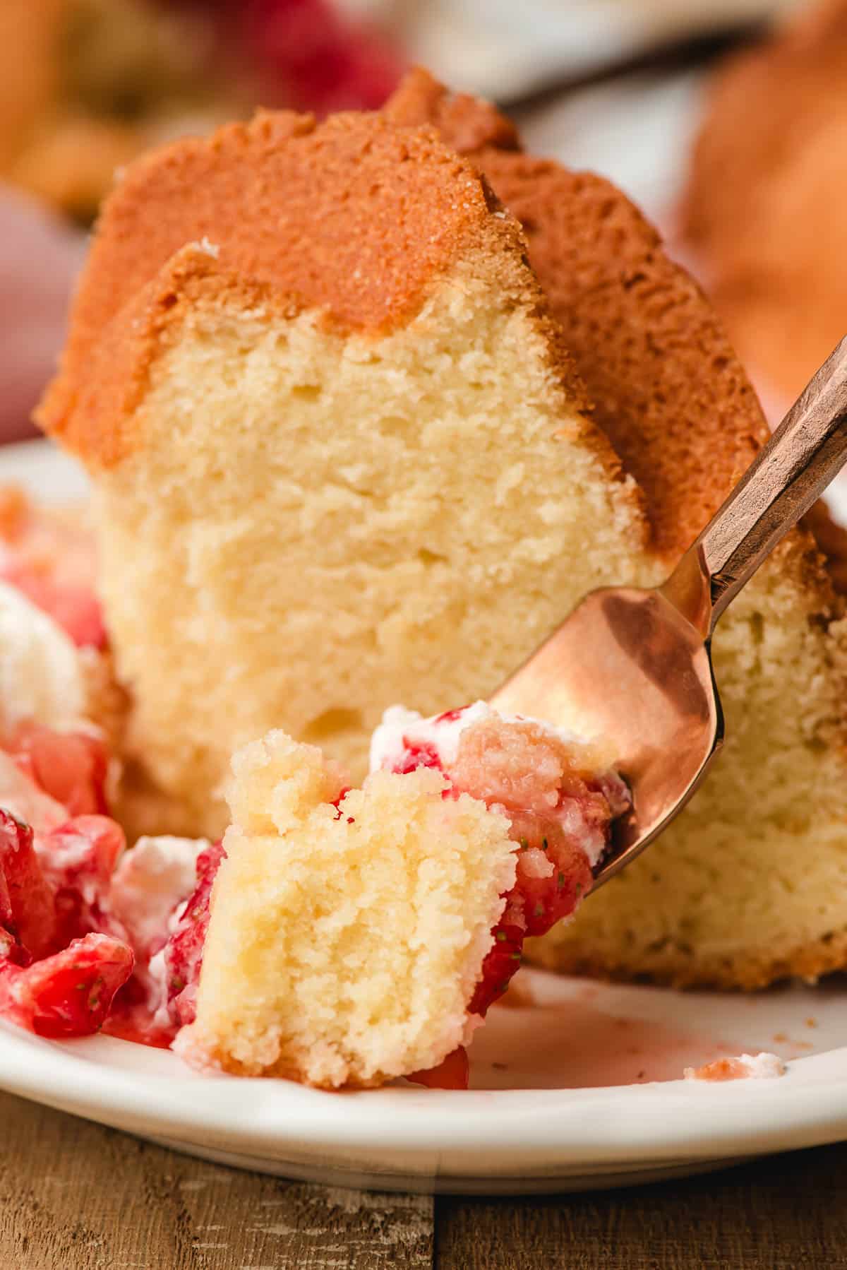 A bite of old fashioned pound cake with strawberries and whipped cream on a golden fork.