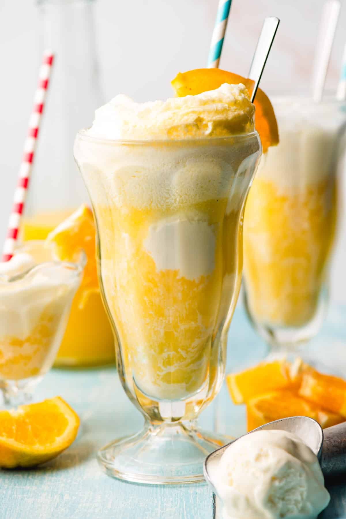 Orange ice cream floats in tall glasses with orange wedge and paper straw.