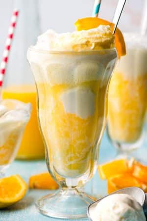 Tall glass filled with bubbly orange float amd topped with a long spoon and paper straw.