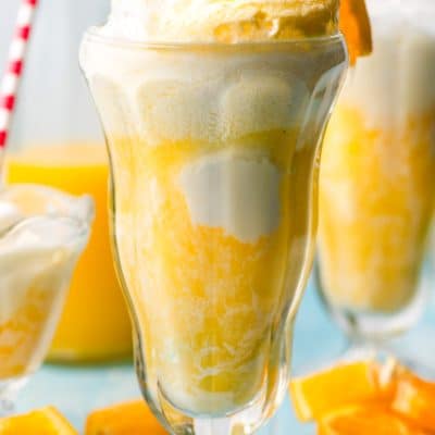 Tall glass filled with bubbly orange float amd topped with a long spoon and paper straw.
