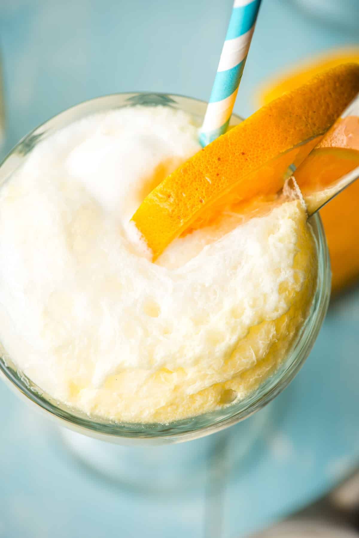 The frothy, bubbly top of an orange float, garnished with an orange wedge.