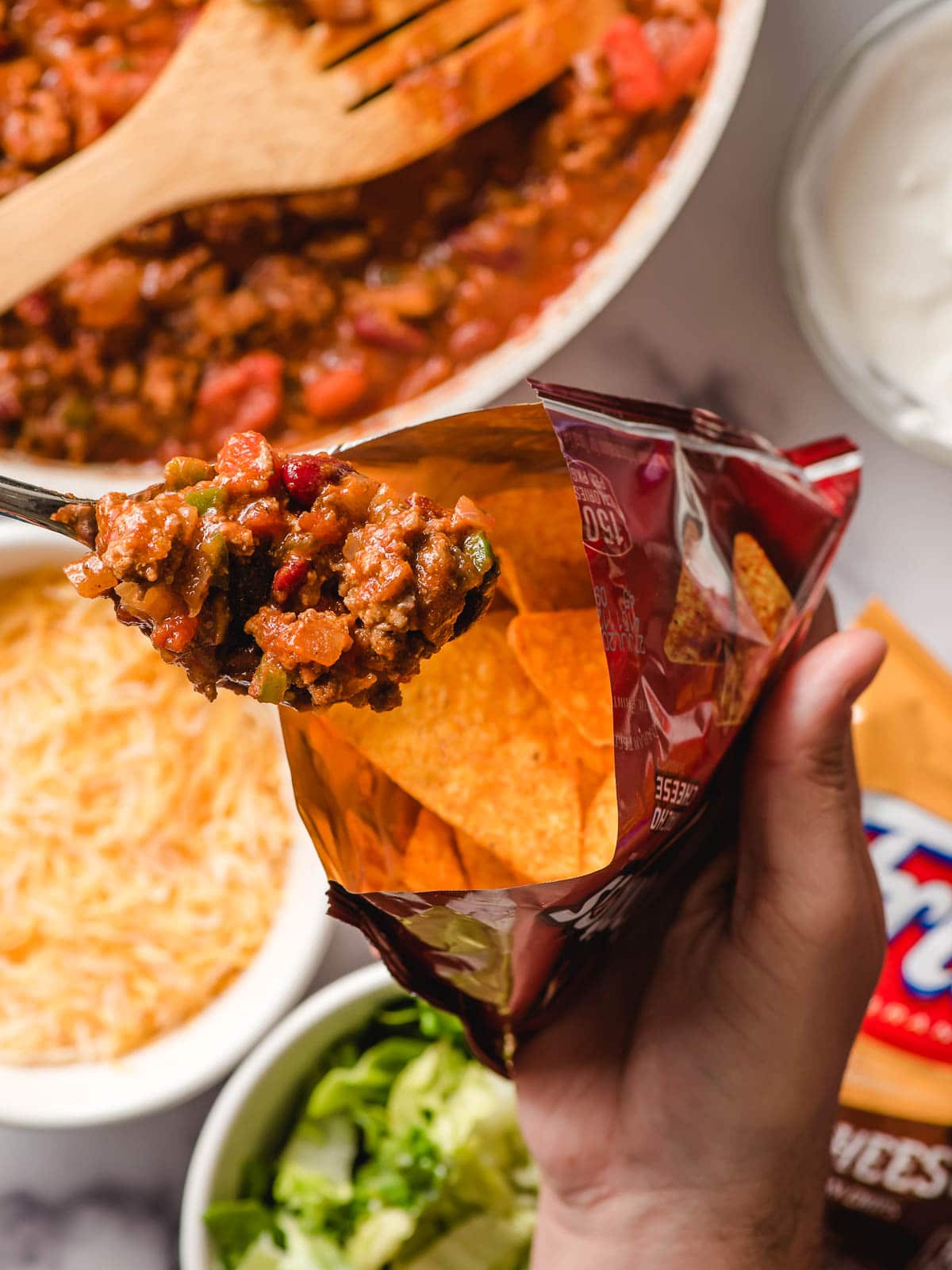 Spoon scooping taco meat into a bag of Doritos.